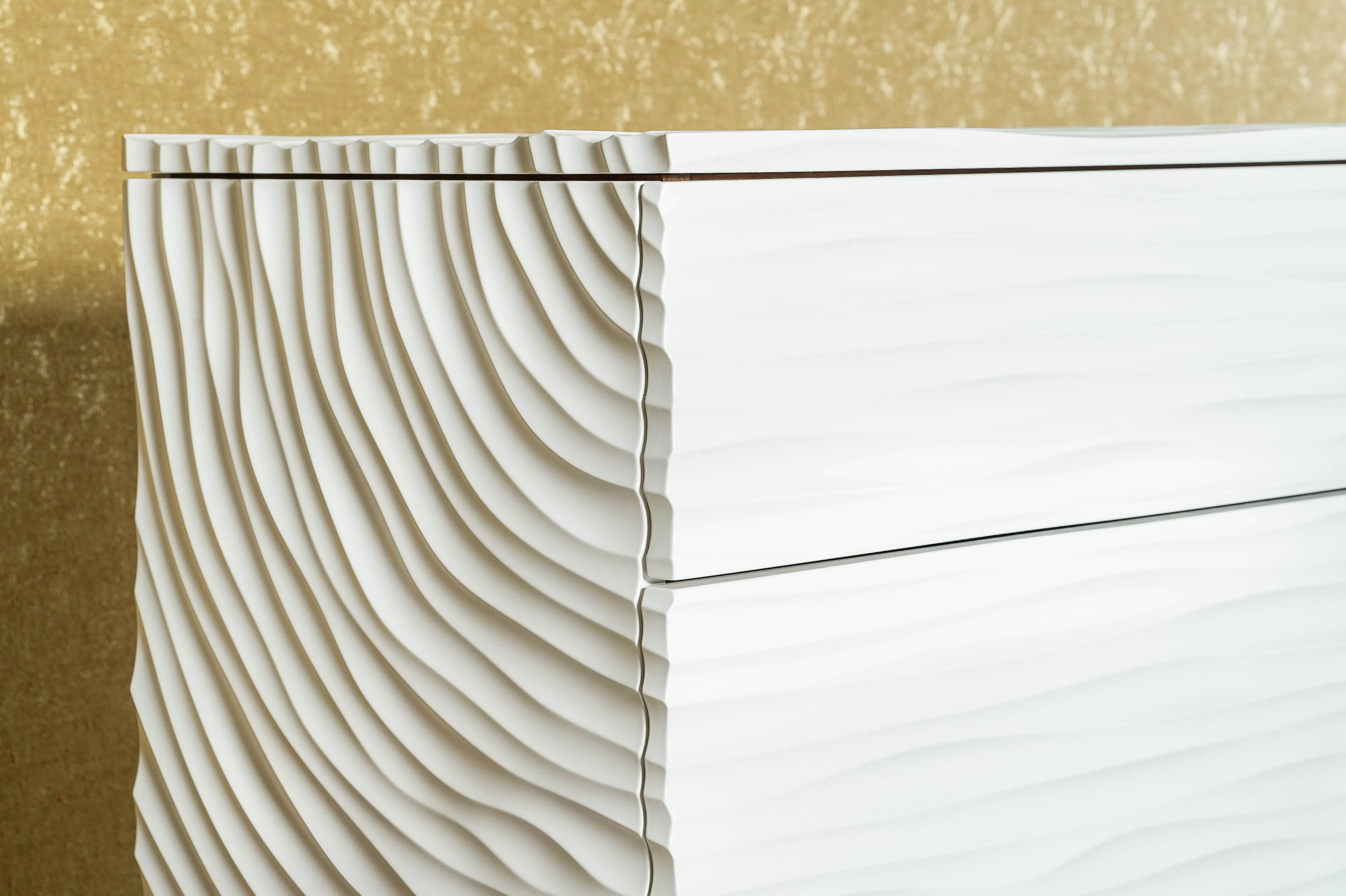 Wave — die gewellte, weiß lackierte Front der Kommode vor goldener Wand